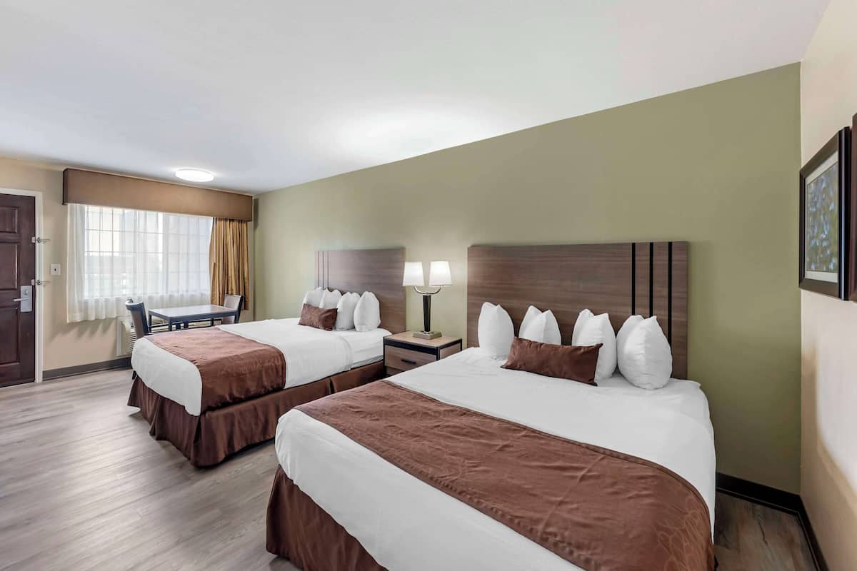 A hotel room with two beds, a desk, and a chair.