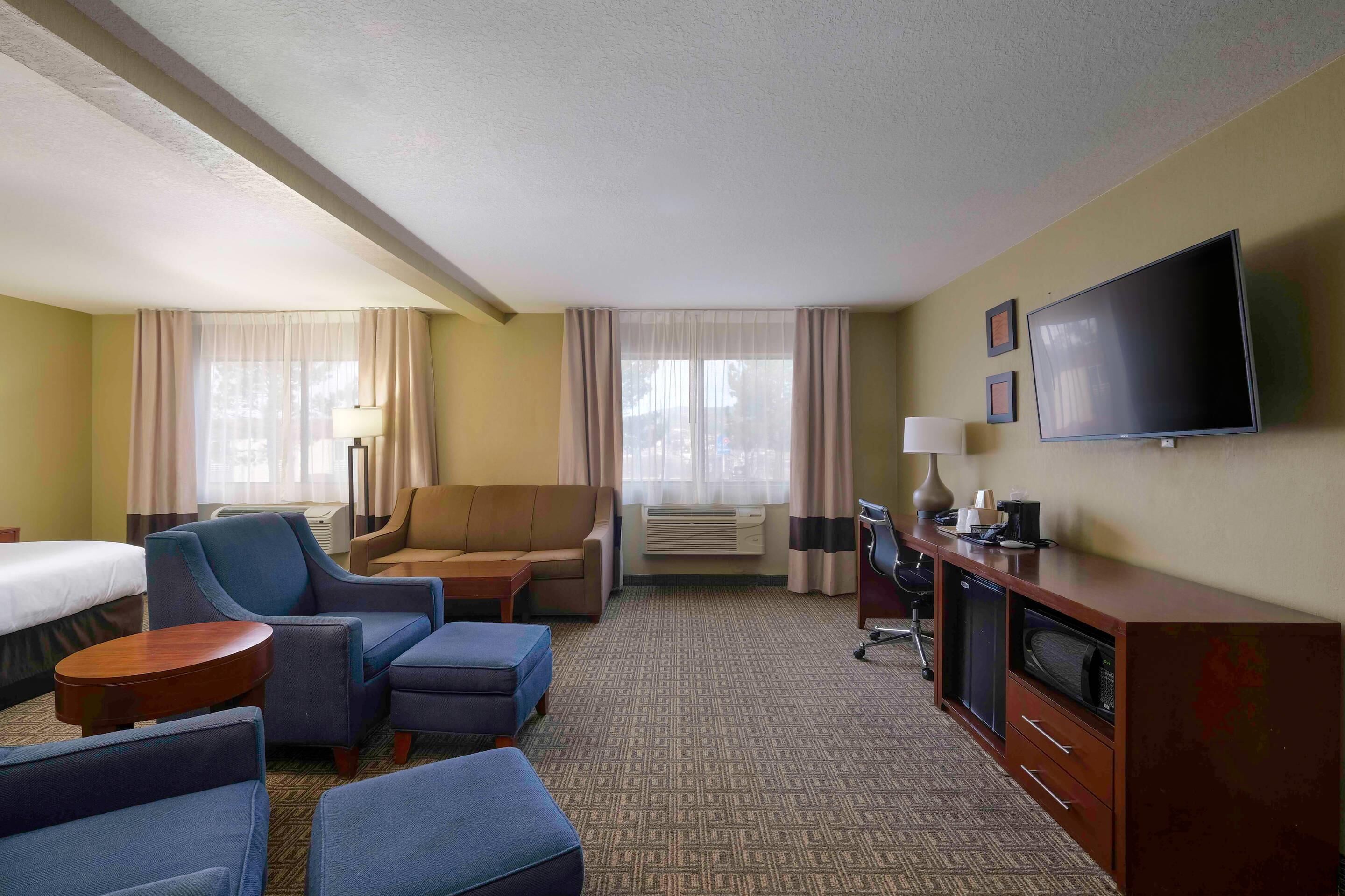 A hotel room with a bed, two sofas, a TV, a desk, and a carpeted floor.