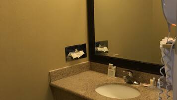 A bathroom with a granite countertop, a sink, a mirror, a hairdryer, and a towel dispenser.