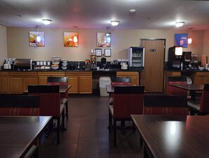 Um restaurante com mesas e cadeiras de madeira, uma máquina de café e um refrigerador.