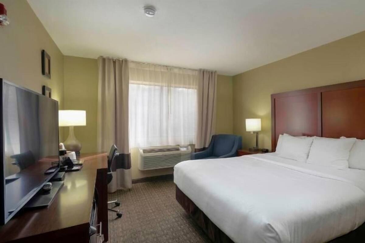 A hotel room with a bed, a desk with a computer, a chair, a television, and a window with curtains.