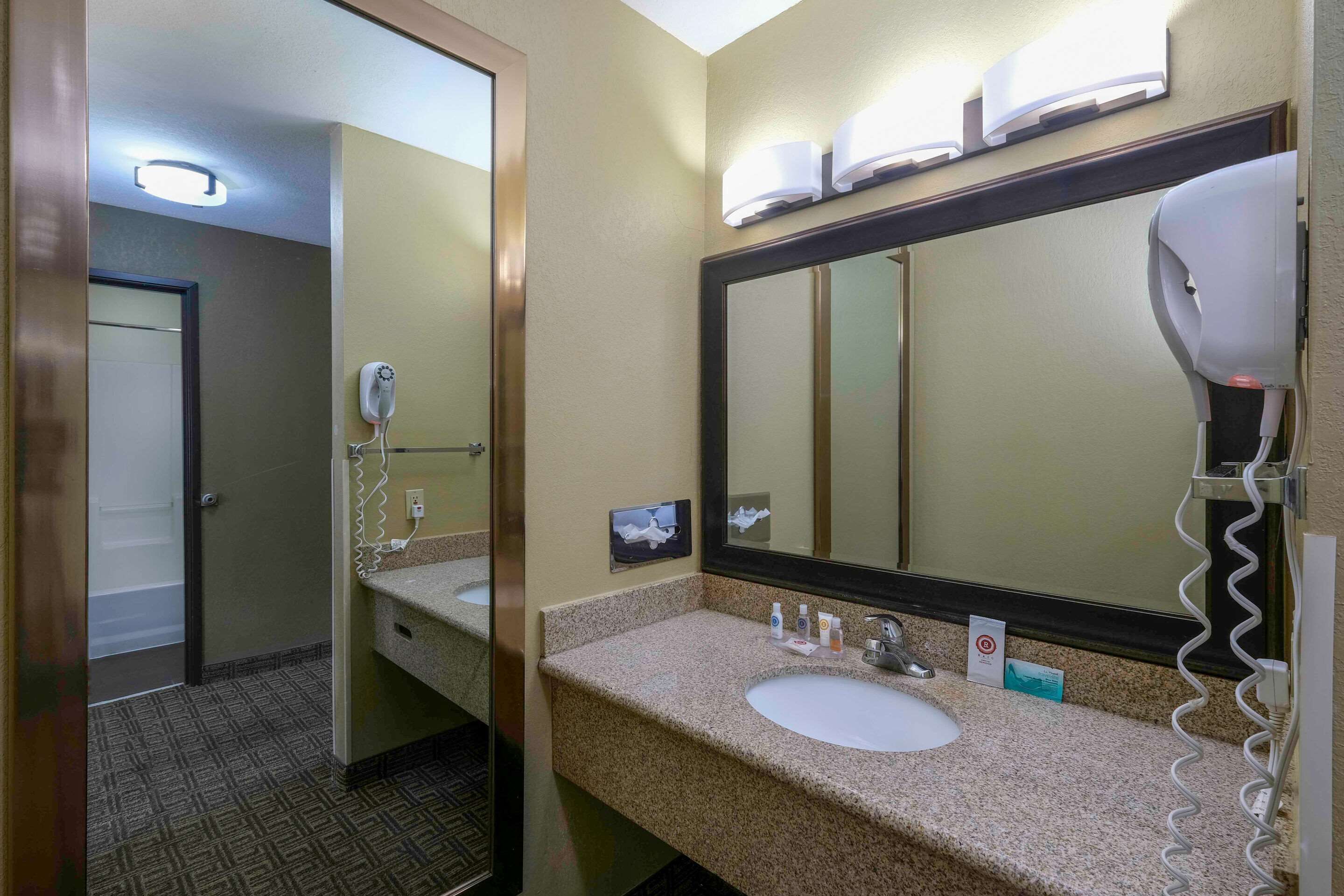 A hotel bathroom with a sink, mirror, hairdryer, and a towel rack.
