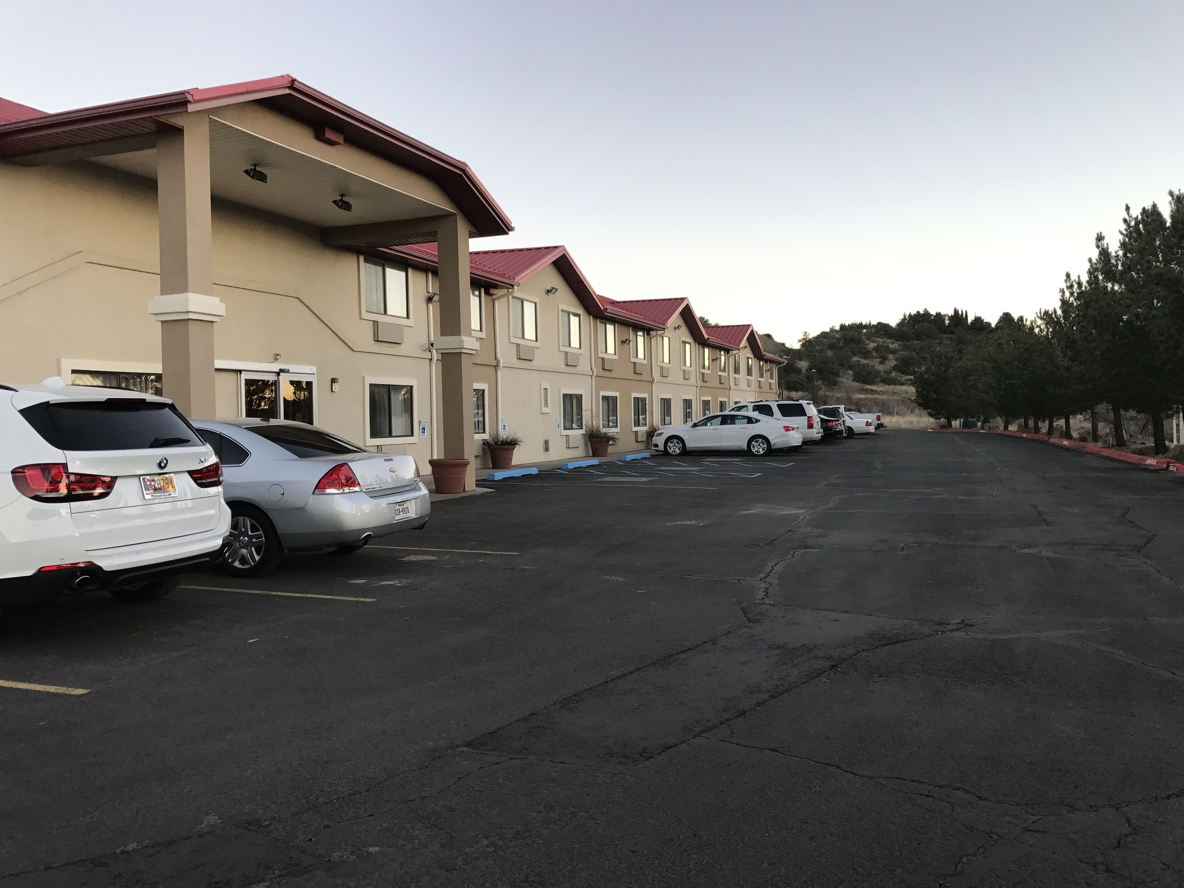 A parking lot with several cars parked in front of a building with a red roof and beige walls.