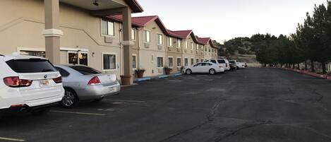 A parking lot with several cars parked in front of a building with a red roof and beige walls.