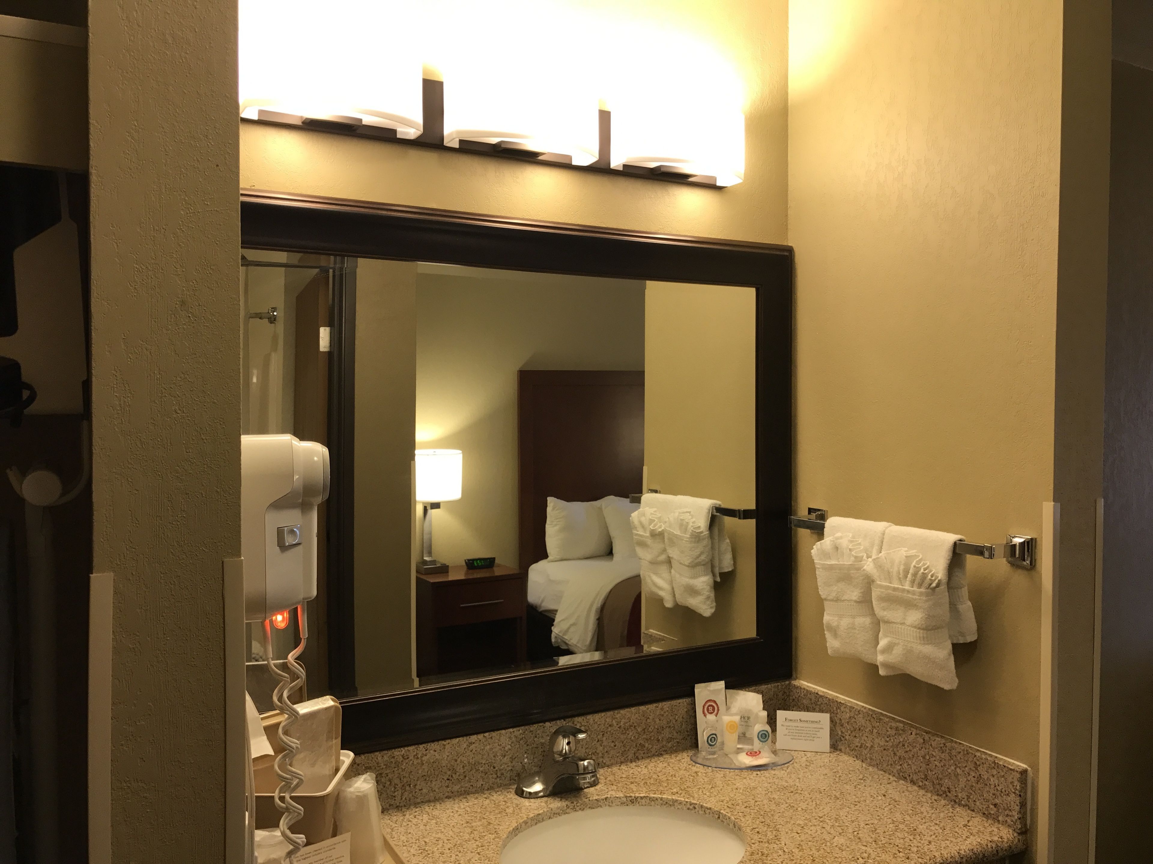 A hotel bathroom with a large mirror, a sink, a towel rack, and a hand dryer.