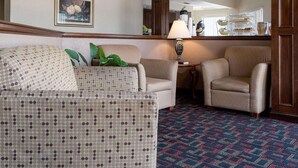 A hotel lobby with a patterned sofa, two armchairs, a coffee station, and a ceiling fan. - Quality Inn Magee (Magee)