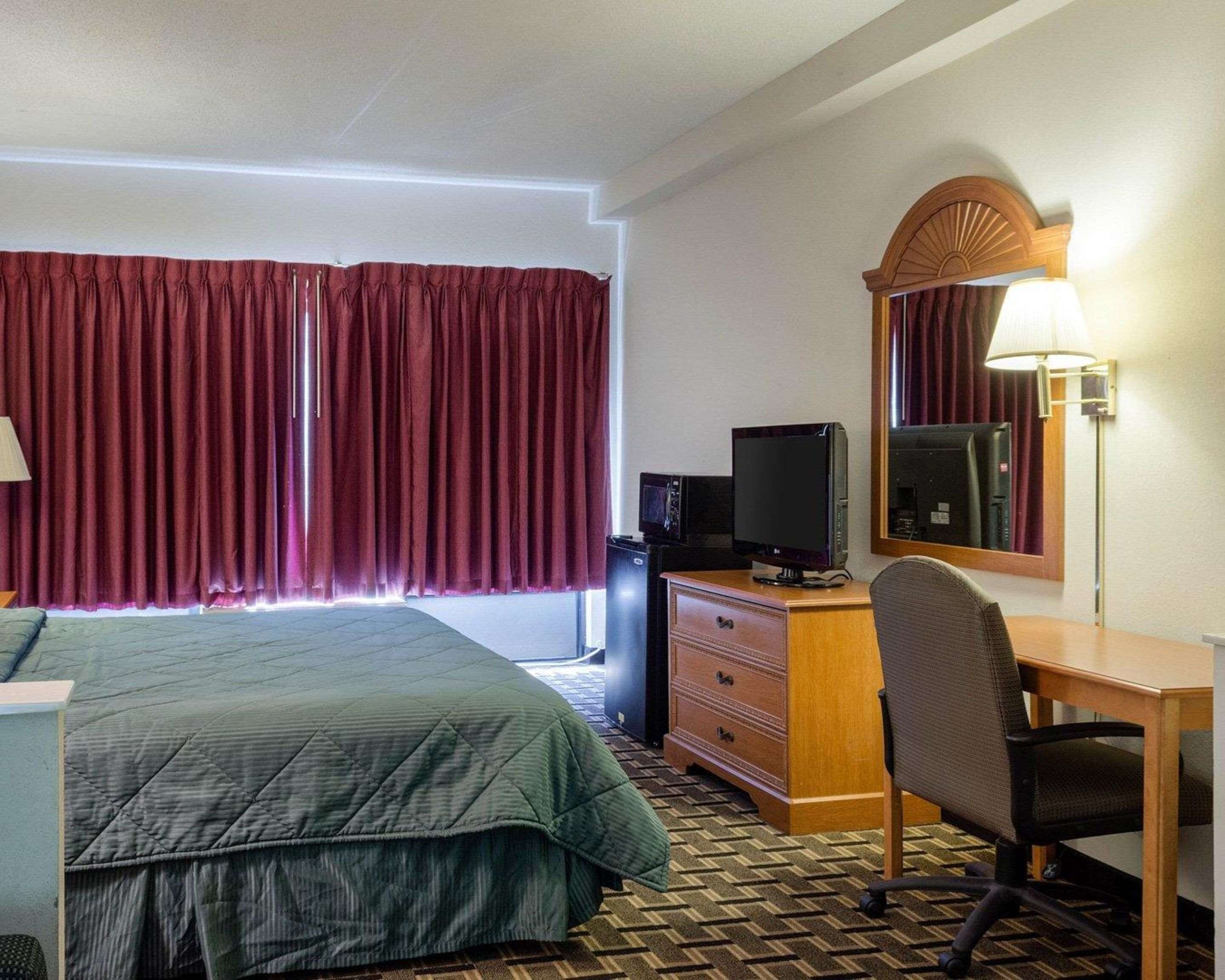 Une chambre d’hôtel équipée d’un lit, d’un bureau avec un ordinateur, d’une télévision, d’un miroir et d’une lampe.