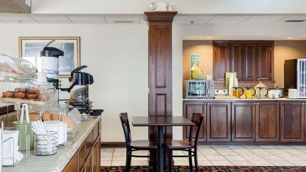 A hotel breakfast area with a buffet, a coffee machine, and a microwave. There is a dining table with chairs and a patterned carpet. - Quality Inn Magee (Magee)