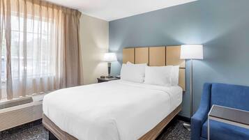 A hotel room with a large bed, a desk with a lamp, a chair, and a window with curtains.