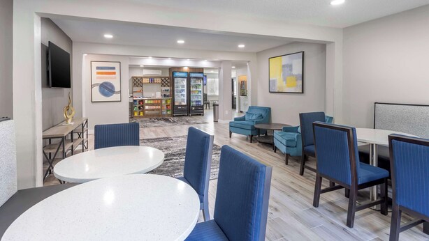 A modern hotel lobby with a round dining table, blue upholstered chairs, a flat-screen TV, and a bookshelf with various items. - Executive Residency by Best Western Philadelphia-Willow Grove (Horsham)