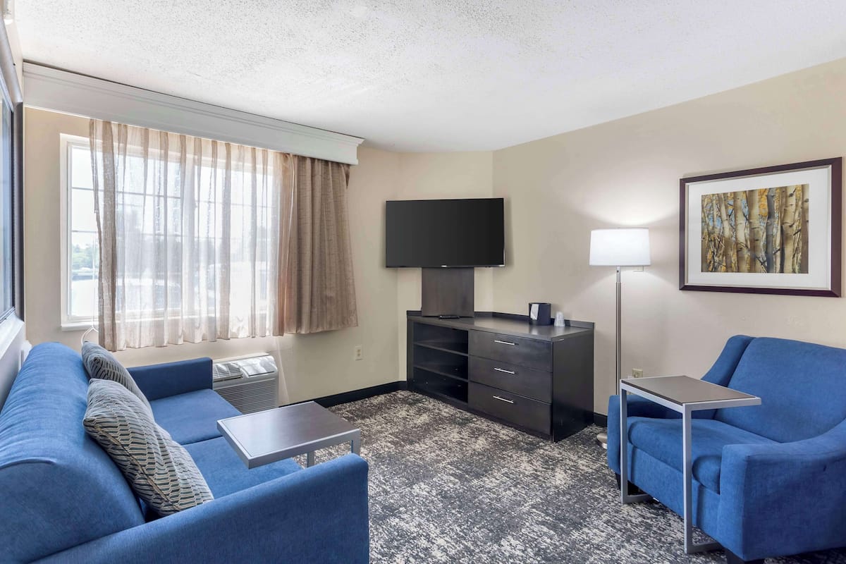 A hotel room with a blue sofa, a small table, a TV on a stand, a lamp, and a framed picture on the wall.