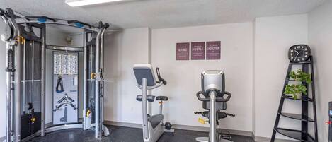 A gym with various exercise equipment, a wall clock, and motivational posters.