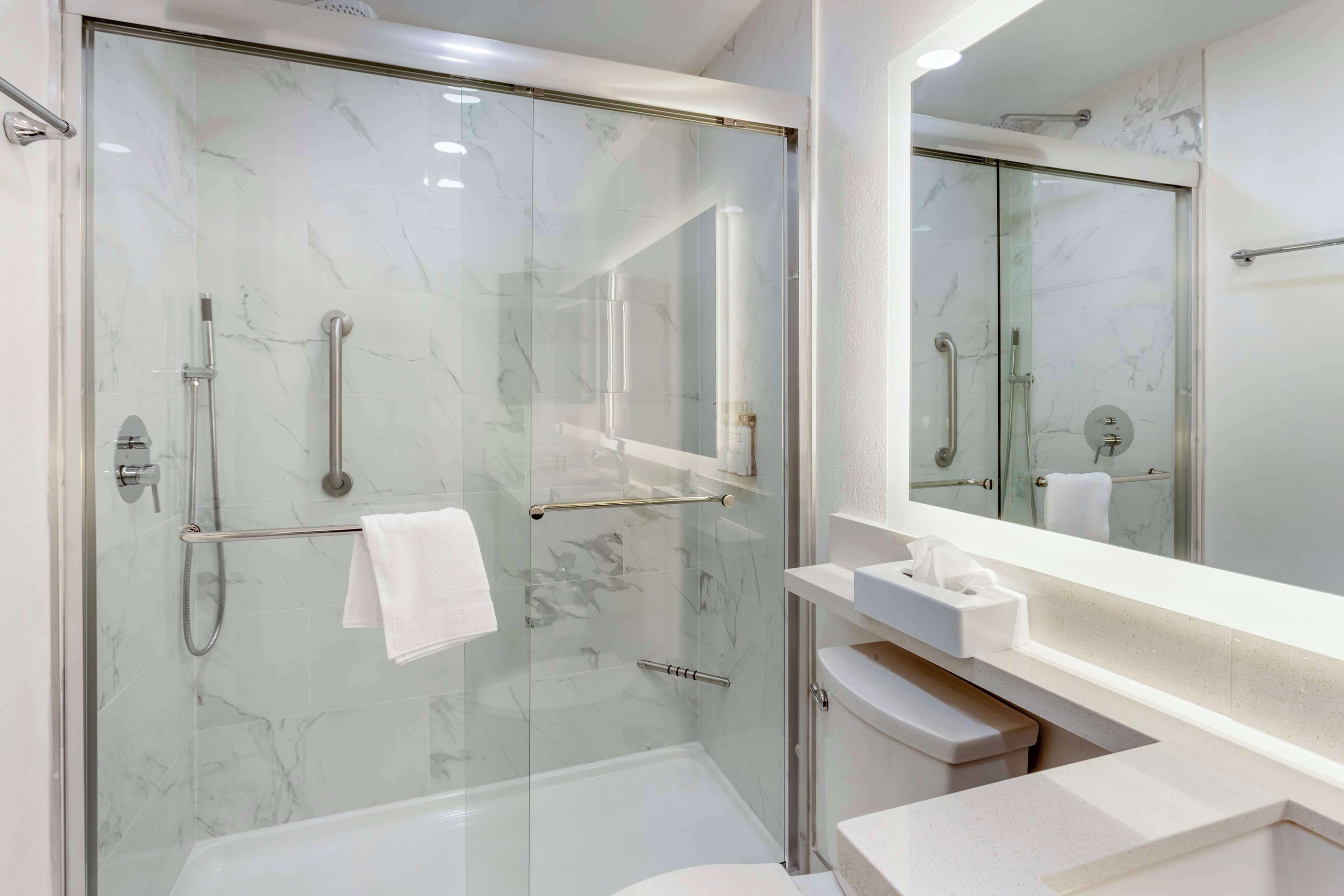 A modern bathroom with a glass-enclosed shower, a white sink, and a large mirror.