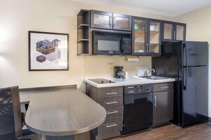 A modern kitchen with a microwave, refrigerator, and dishwasher. There is a dining table with chairs and a framed picture on the wall.