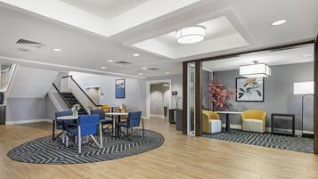 Um hall de hotel espaçoso com teto alto, escadaria e área de estar com mesas e cadeiras.
