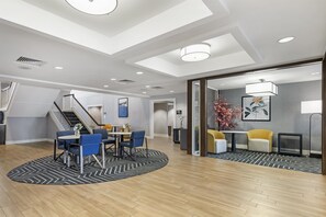 A spacious hotel lobby with a high ceiling, a staircase, and a seating area with tables and chairs.