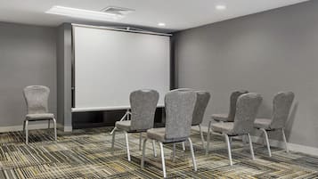 A conference room with a whiteboard, grey upholstered chairs, and patterned carpet.