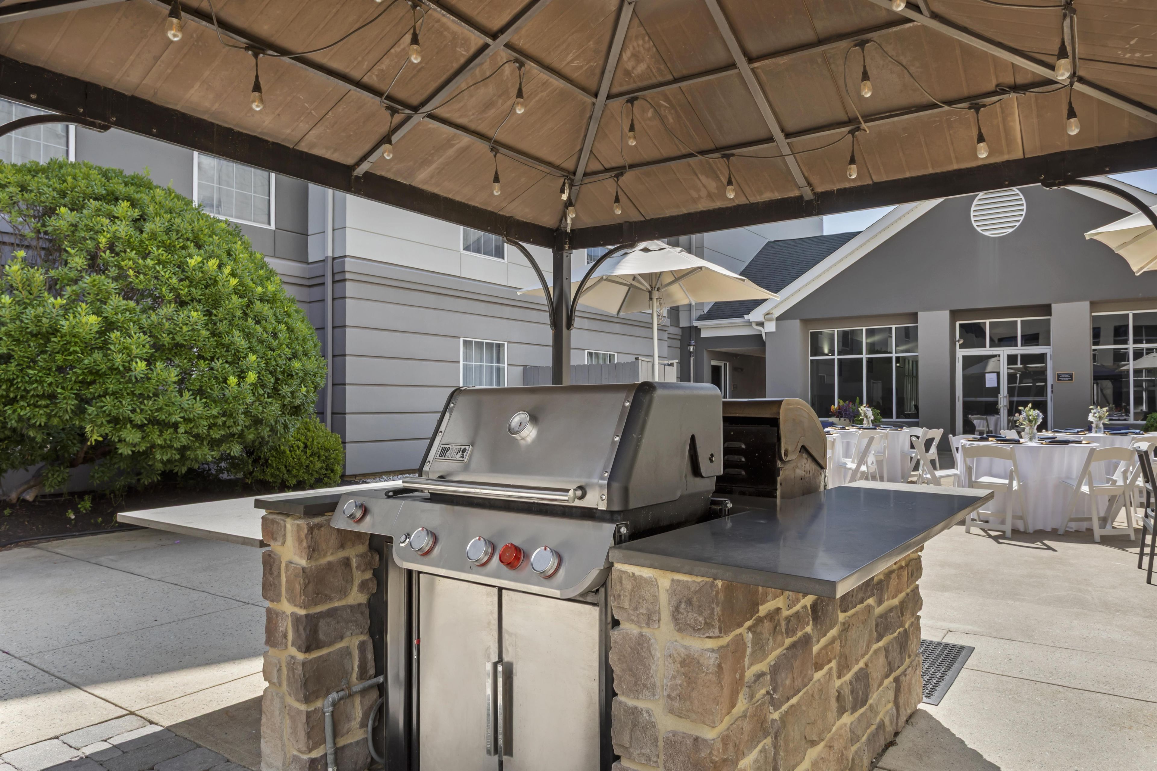 Een buitengrillplaats met een stenen constructie, een tafel met stoelen en een overdekte zithoek.