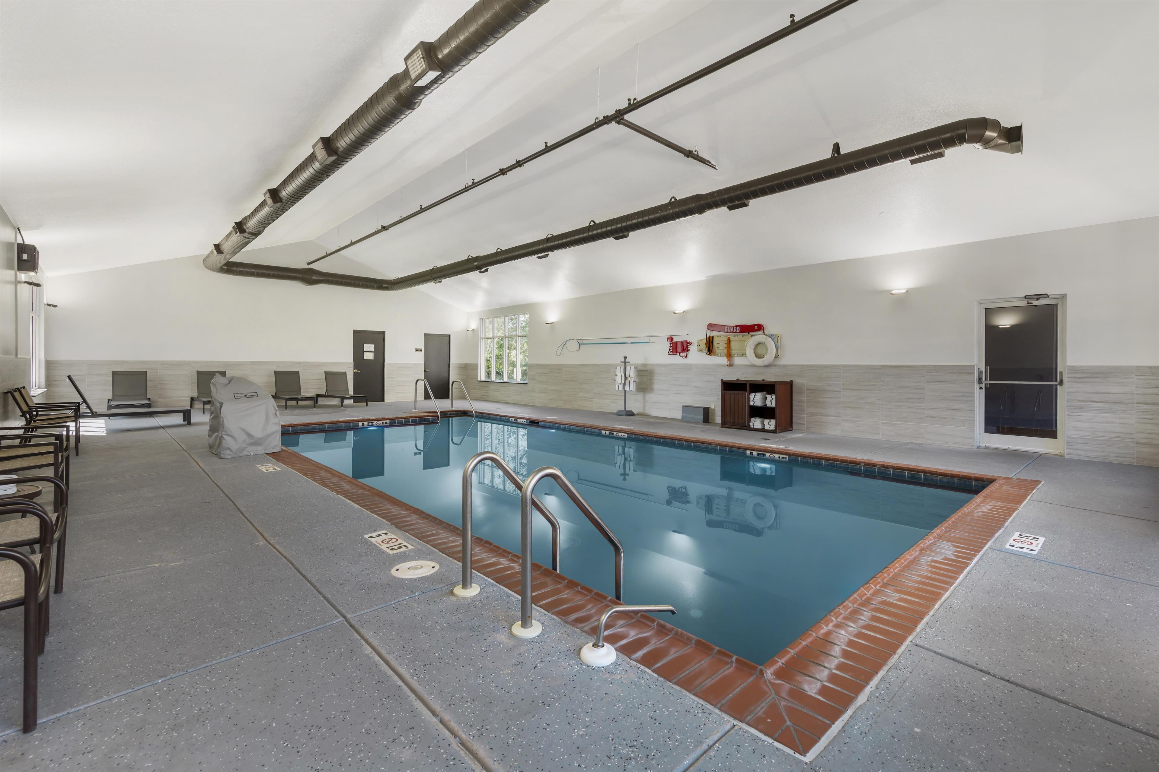 Una piscina con solárium de baldosas, barandillas metálicas y puesto de socorrista.