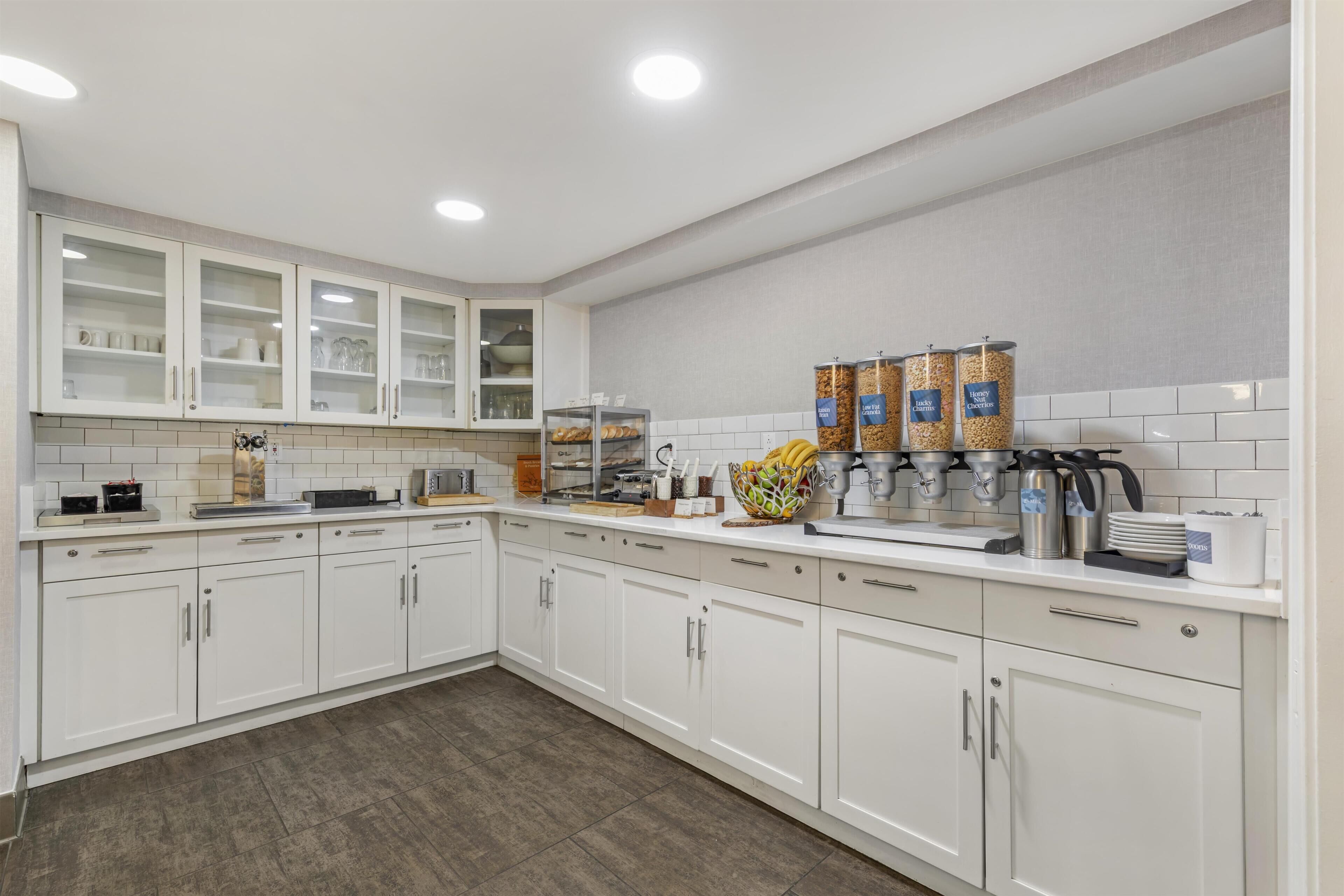 A modern kitchen with white cabinets, a coffee station, and a fruit bowl.