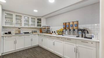A modern kitchen with white cabinets, a coffee station, and a fruit bowl.