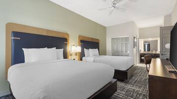 A hotel room with two beds, a desk, a chair, a television, and a ceiling fan.