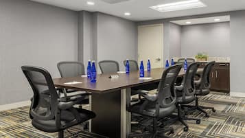 Un salón de conferencias con una larga mesa, seis sillas y botellas de agua azules sobre la mesa.