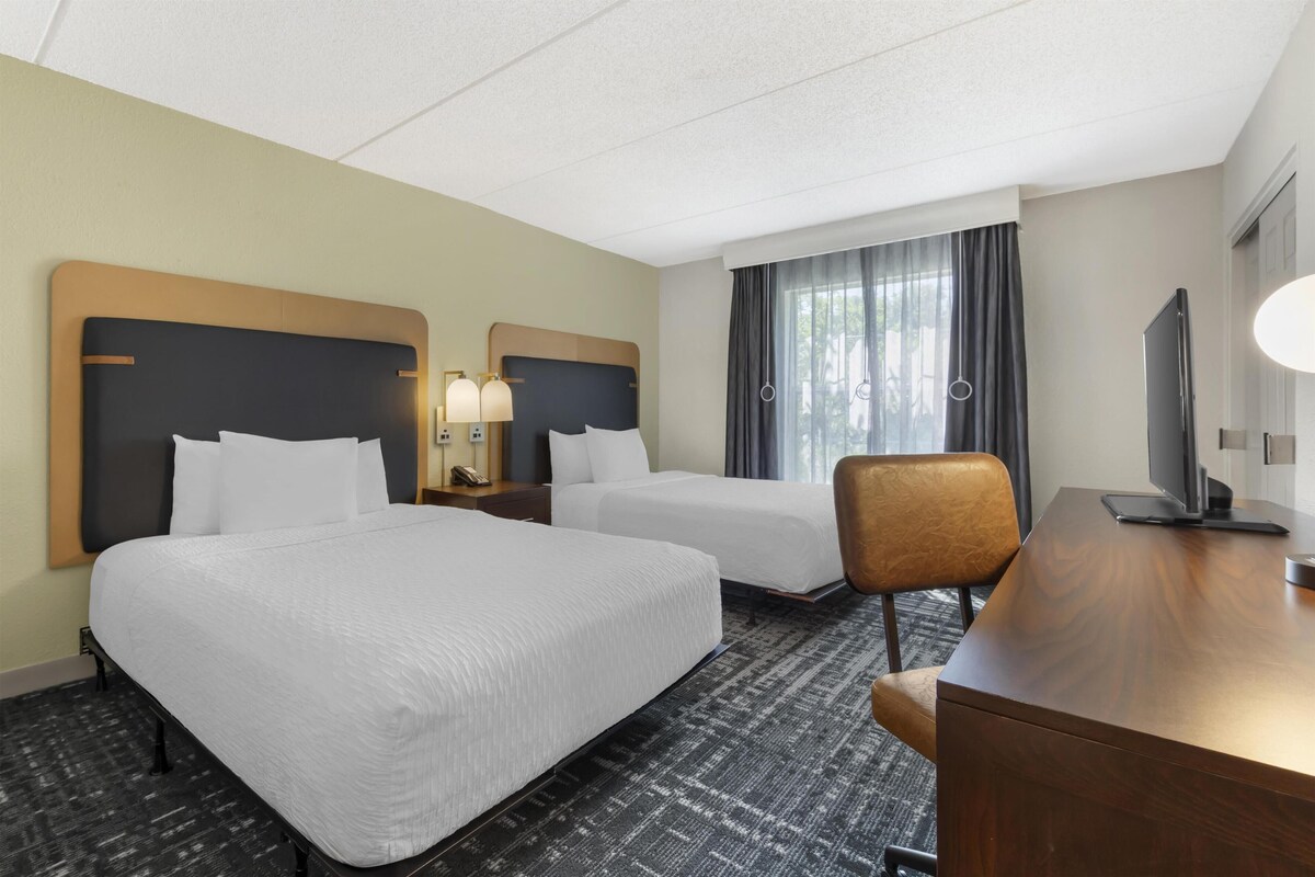 A hotel room with two beds, a desk, a chair, a TV, and a window with curtains.