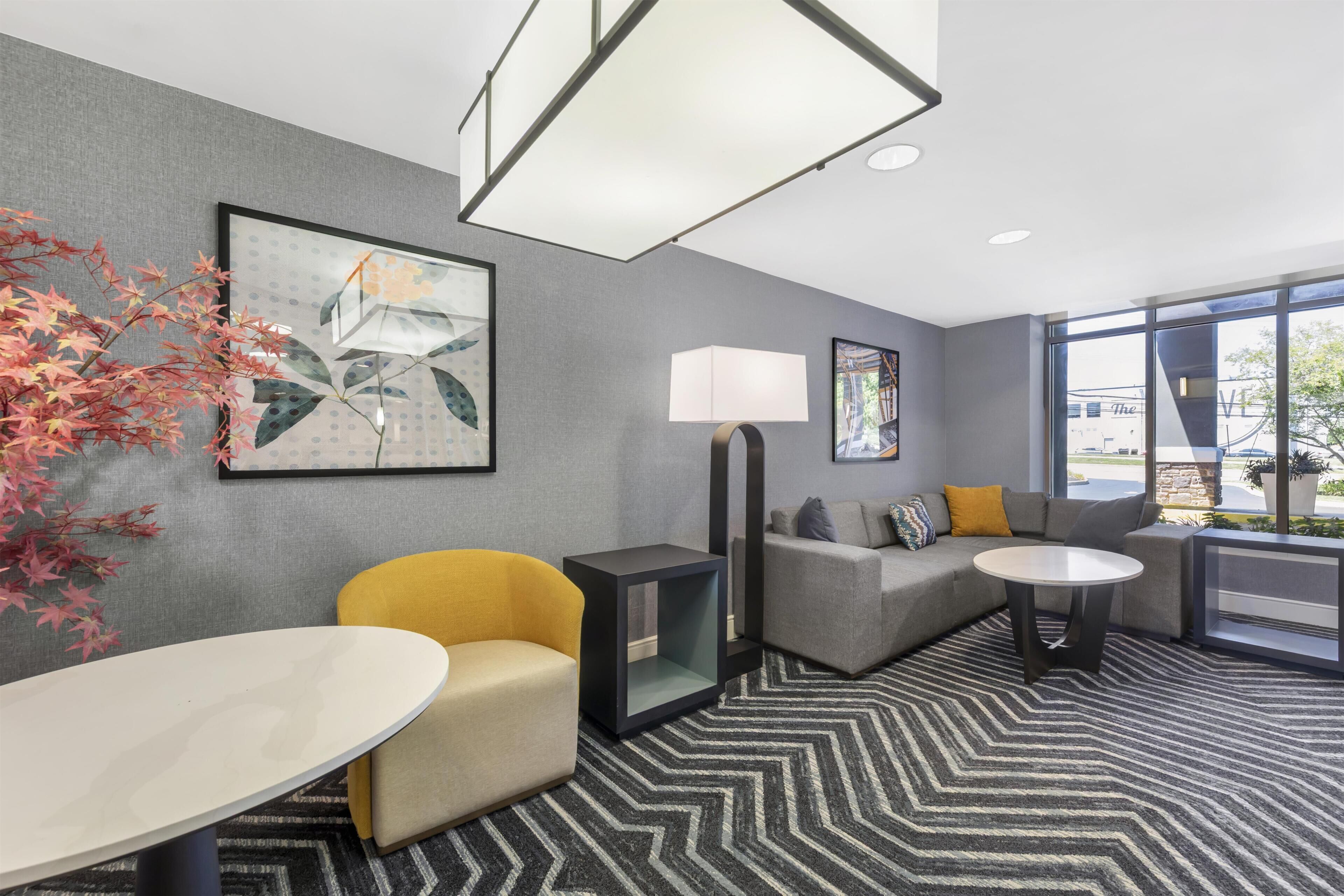 Una habitación de hotel moderna con sofá, sillón y una pequeña mesa. Hay un ventanal que ofrece vistas al exterior.