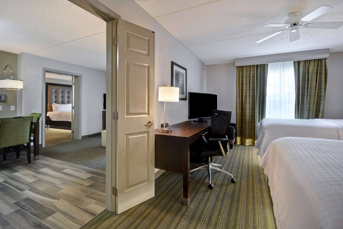 A hotel room with a bed, desk, chair, television, and a door leading to another room.