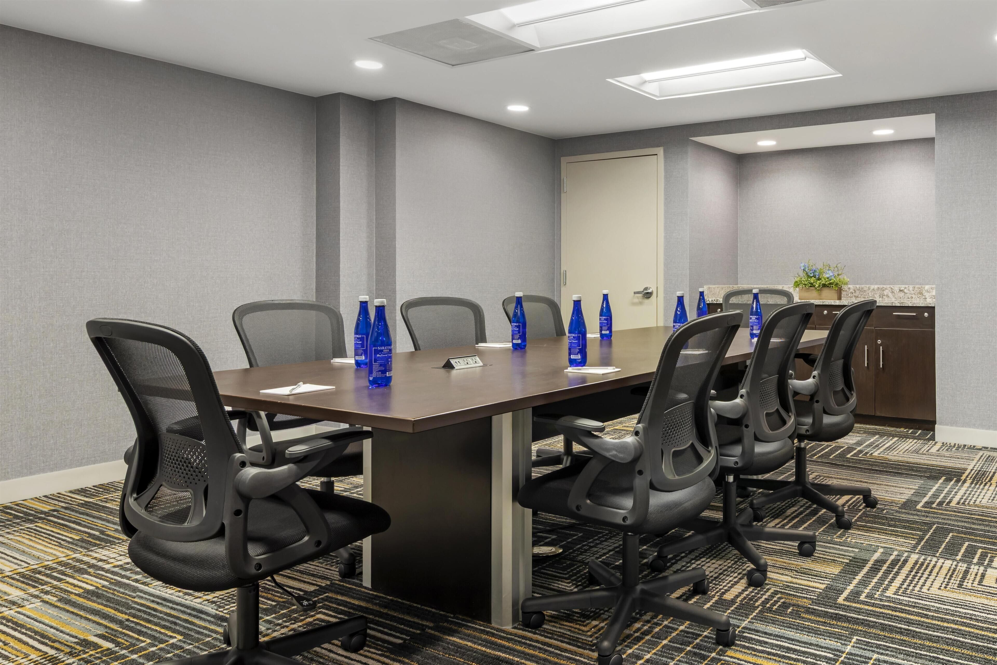A conference room with a long table, six chairs, and blue water bottles on the table.