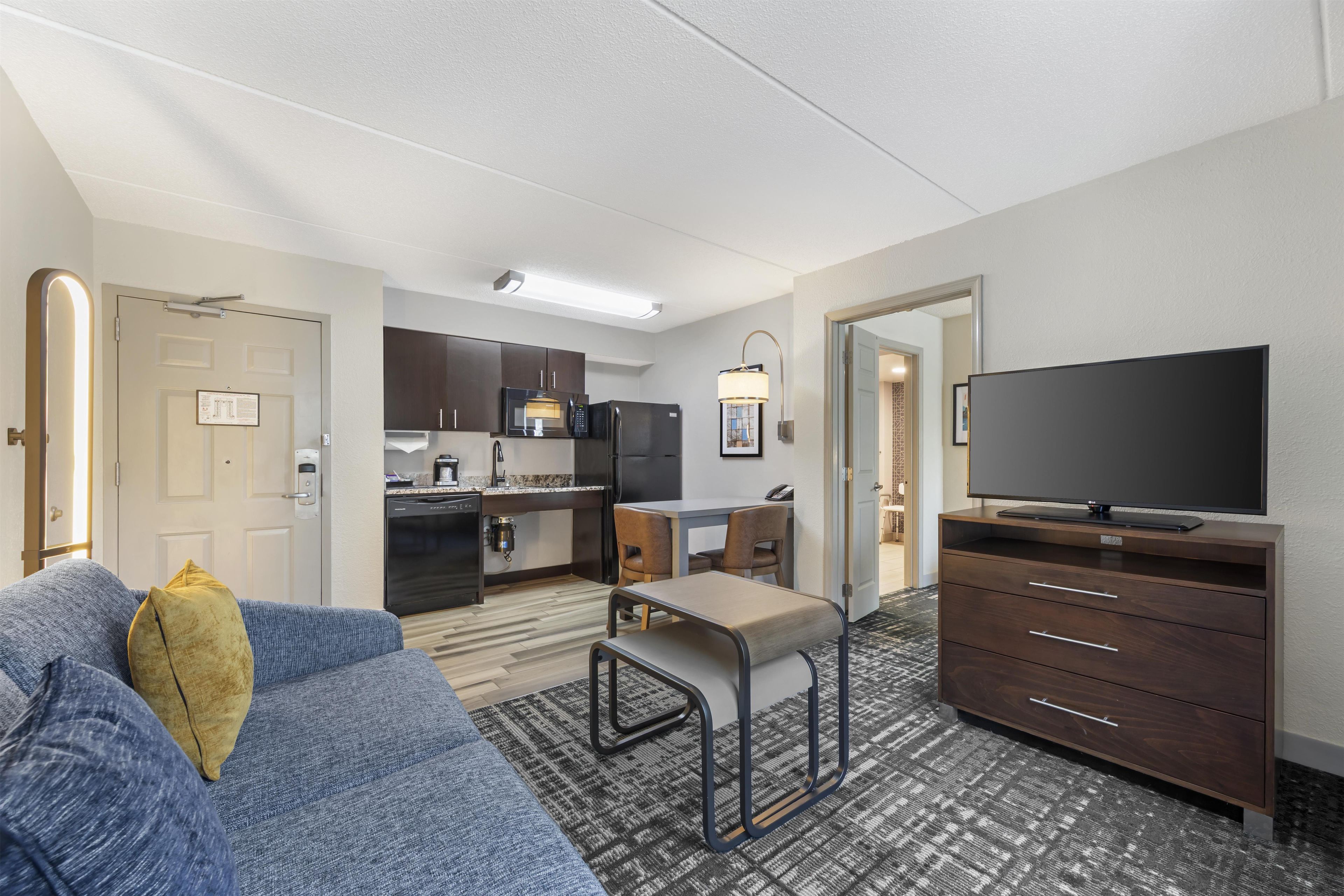 Een moderne hotelkamer met een bank, een televisie, een kitchenette en een eethoek.