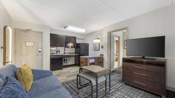 Een moderne hotelkamer met een bank, een televisie, een kitchenette en een eethoek.