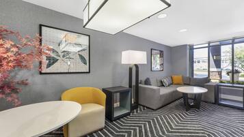 Una habitación de hotel moderna con sofá, sillón y una pequeña mesa. Hay un ventanal que ofrece vistas al exterior.