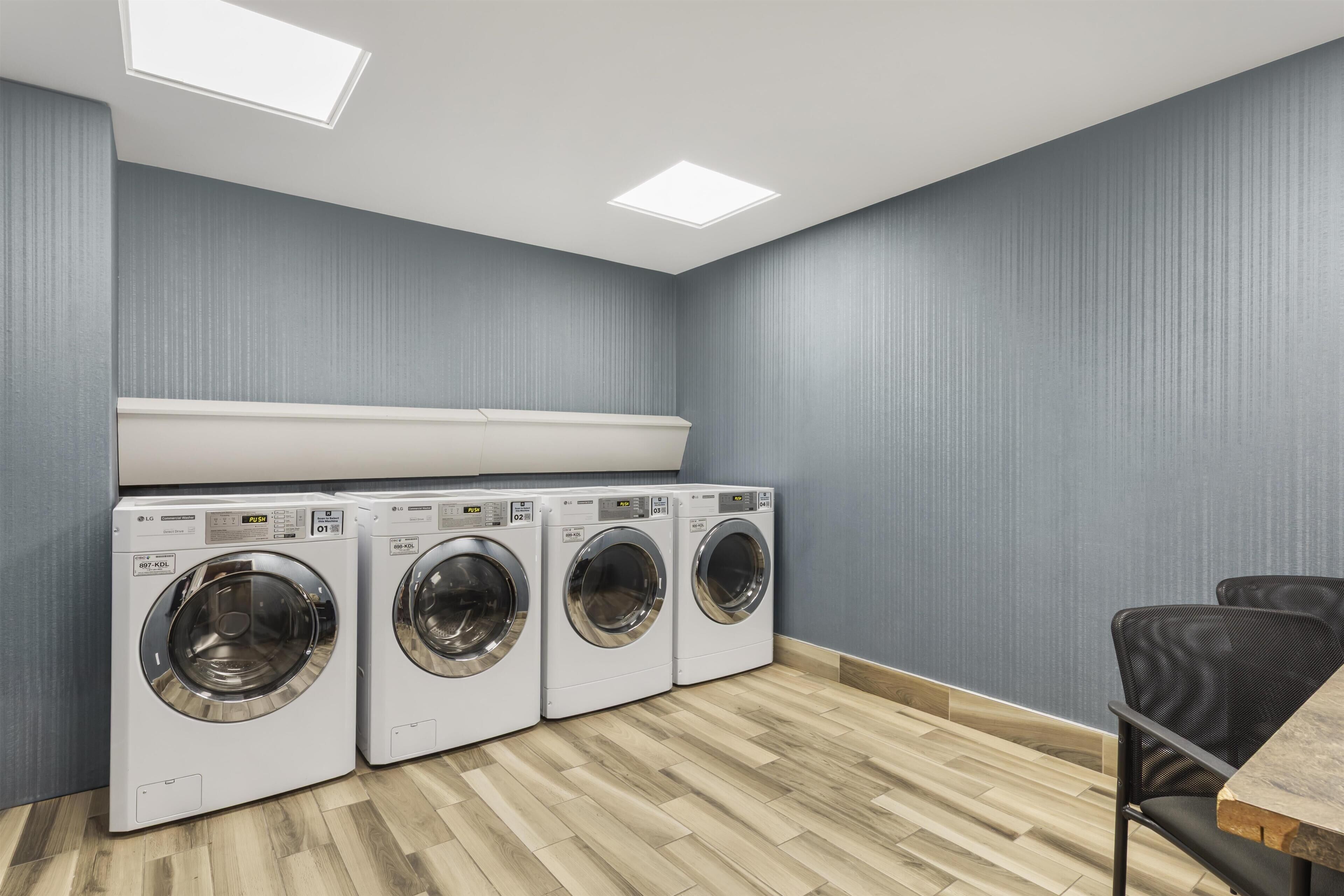 A laundry room with four LG commercial washers, a wooden floor, and a grey wall.