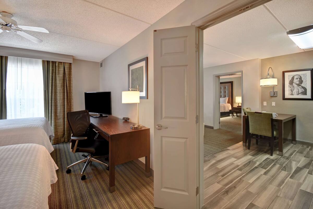 A hotel room with two beds, a desk with a chair, a television, and a door leading to another room.