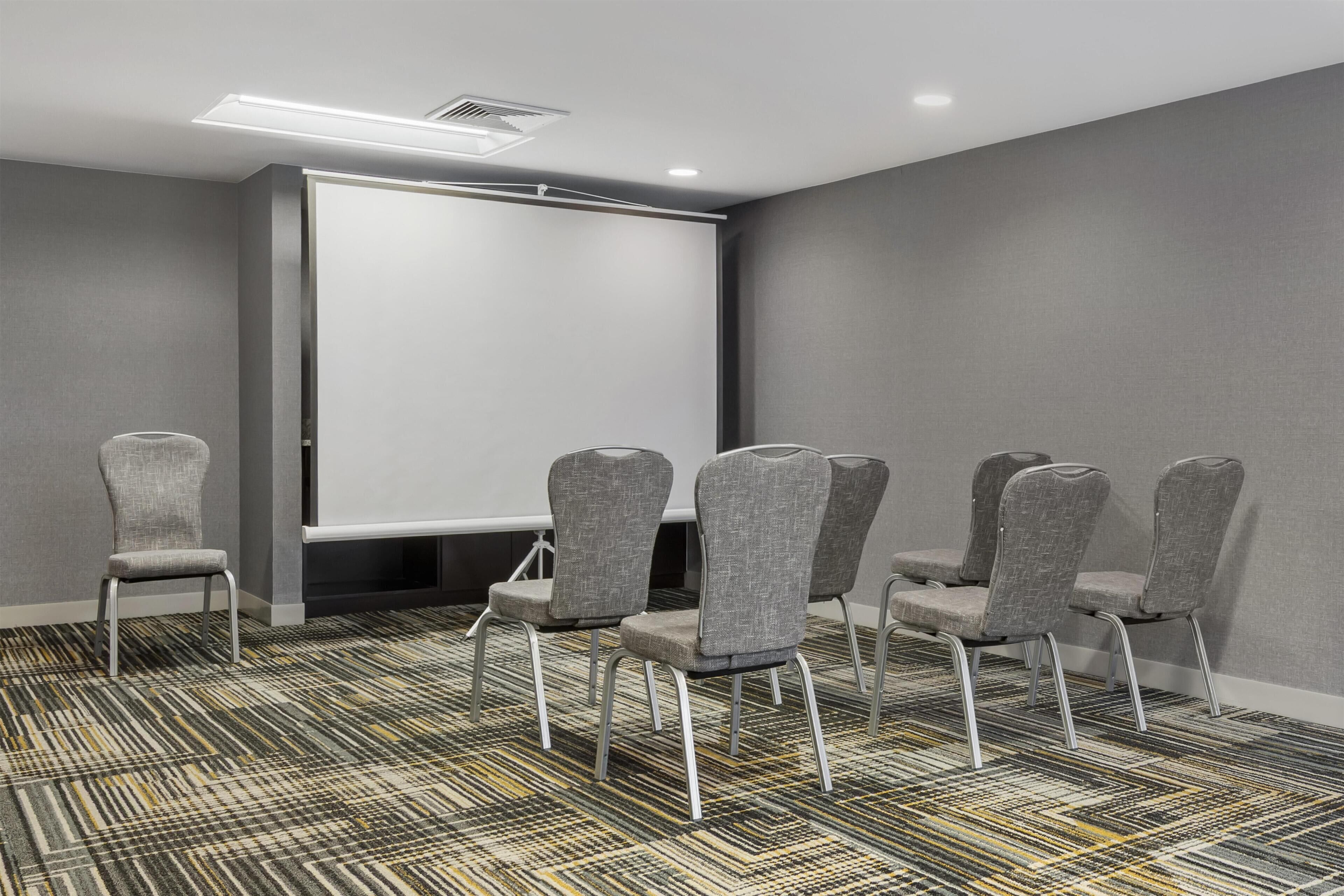 A conference room with a whiteboard, grey upholstered chairs, and patterned carpet.