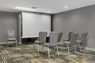Un salón de conferencias con una pizarra, sillas tapizadas grises y alfombra estampada.