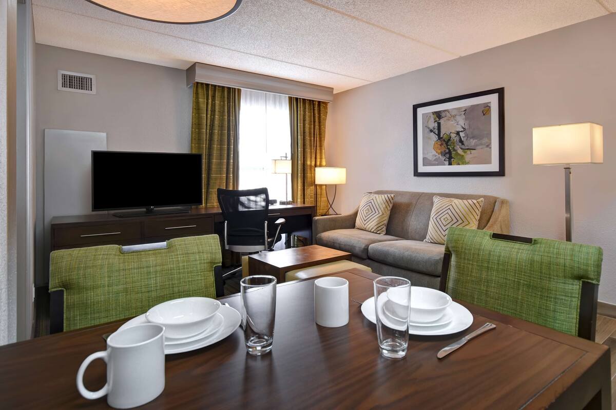 A hotel room with a dining area, a sofa, a TV, and a painting on the wall.