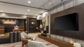 Eine moderne Hotelhalle mit Rezeption, einer Sitzecke und einem großen, an der Wand befestigten Flachbildfernseher.
