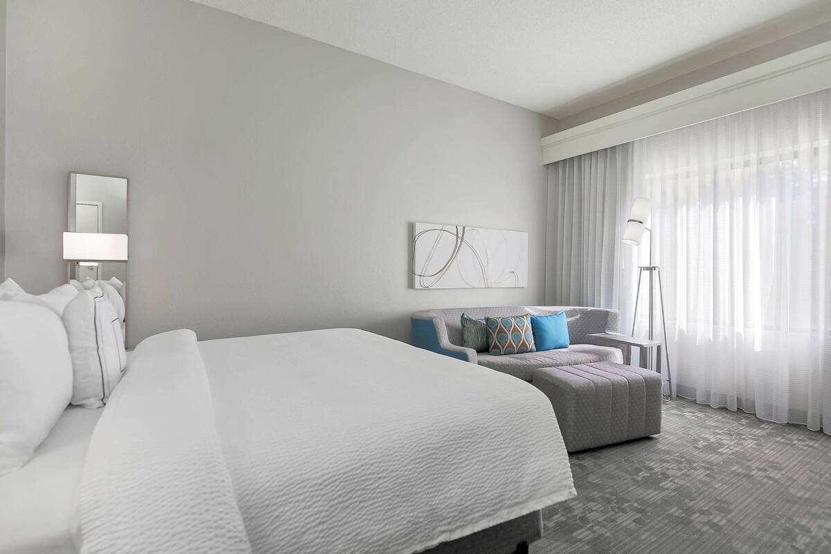 A hotel room with a large bed, a sofa, a desk, and a lamp.