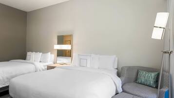 A hotel room with two beds, a sofa, a lamp, and a mirror.