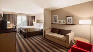 A hotel room with a bed, a desk, a sofa, a red chair, and a round table. - Country Inn & Suites by Radisson, Rock Hill, SC (Rock Hill)