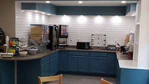 A kitchen with blue cabinets, a microwave, a coffee machine, and a small dining area with a table and chairs. - Country Inn & Suites by Radisson, Rock Hill, SC (Rock Hill)