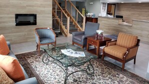 A living room with a sofa, armchairs, a glass coffee table, a patterned rug, a wooden staircase, and a flat-screen TV mounted on the wall. - Country Inn & Suites by Radisson, Rock Hill, SC (Rock Hill)