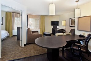 A hotel room with a bed, a seating area with a table and chairs, a television, and a desk with a lamp.