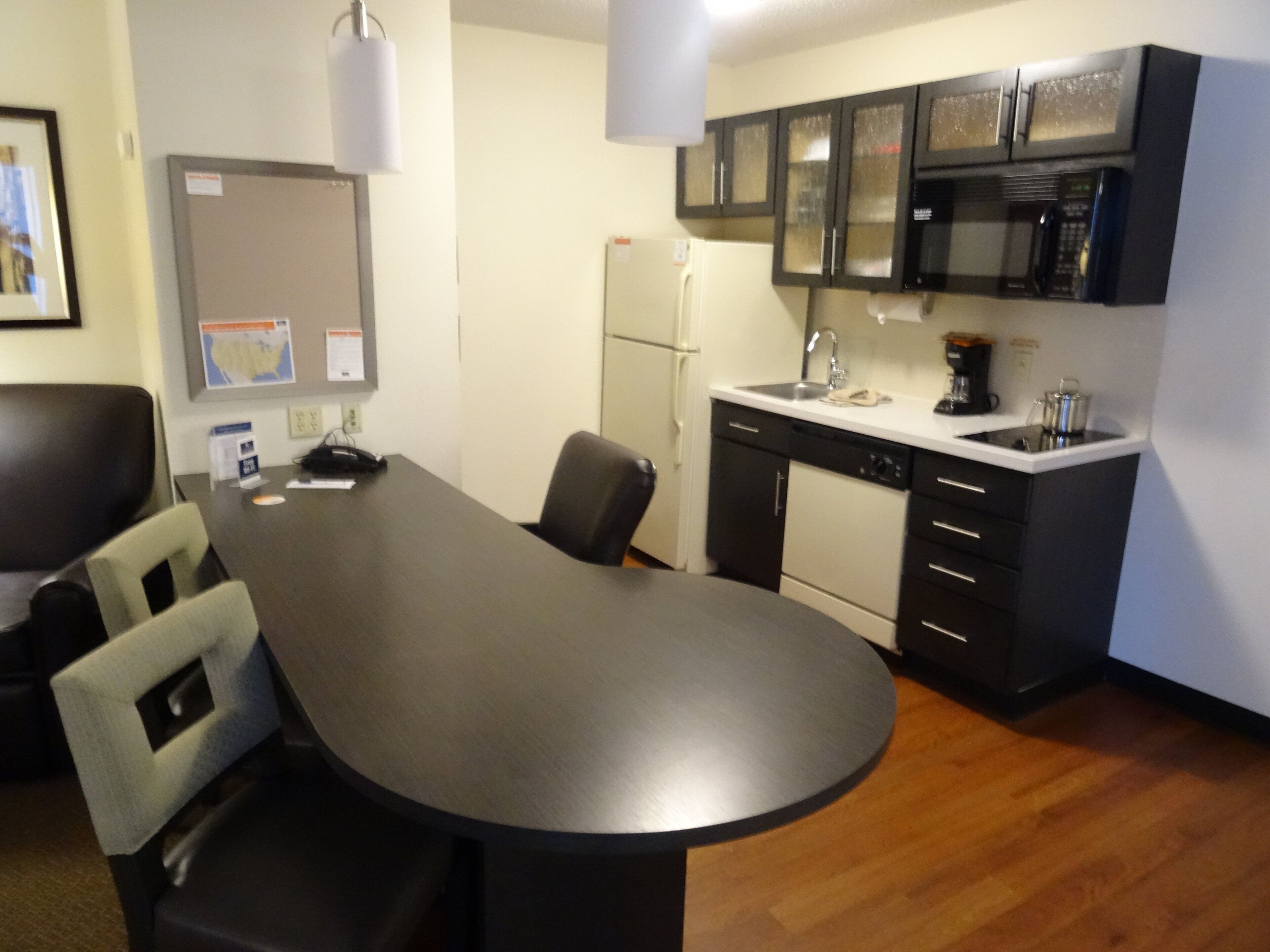 A small kitchen with a refrigerator, microwave, and sink. There is a dining table with chairs.