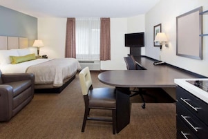 Una habitación de hotel con cama, escritorio, silla, televisor y ventana con cortinas.