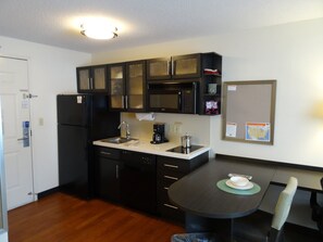 A compact kitchen with a refrigerator, microwave, sink, and a dining table with chairs. - Candlewood Suites Wichita Airport by IHG (Wichita)