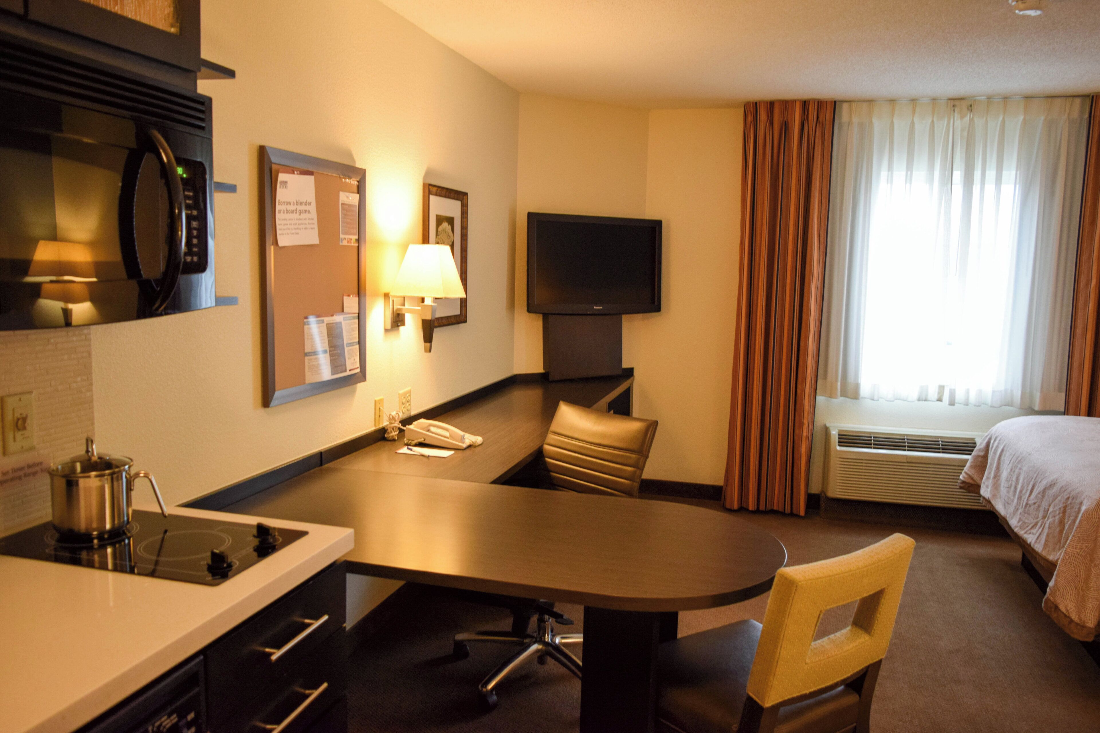 A hotel room with a kitchenette, a flat-screen TV, a bed, and a window with curtains.
